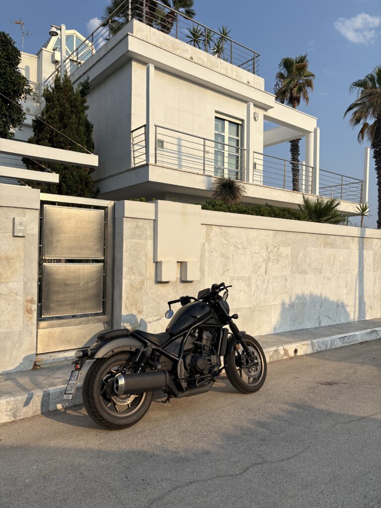 A beautiful white, concrete home with a black motorcycle parked on the street outside. There are palm trees and a metal gate. Illustrating the masculine home interior and exterior design elements showcased by Tripplehorn Desings in Eagle, Idaho. 